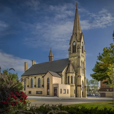 Church exterior with tall Gothic spire, flower beds and a blue sky