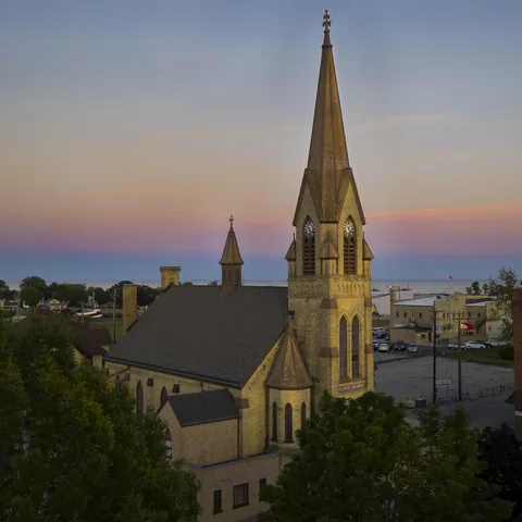 Church spire above trees beneath a pastel evening sky
