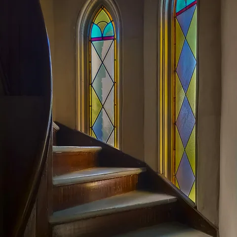 Curved wooden stairs beside tall stained-glass windows